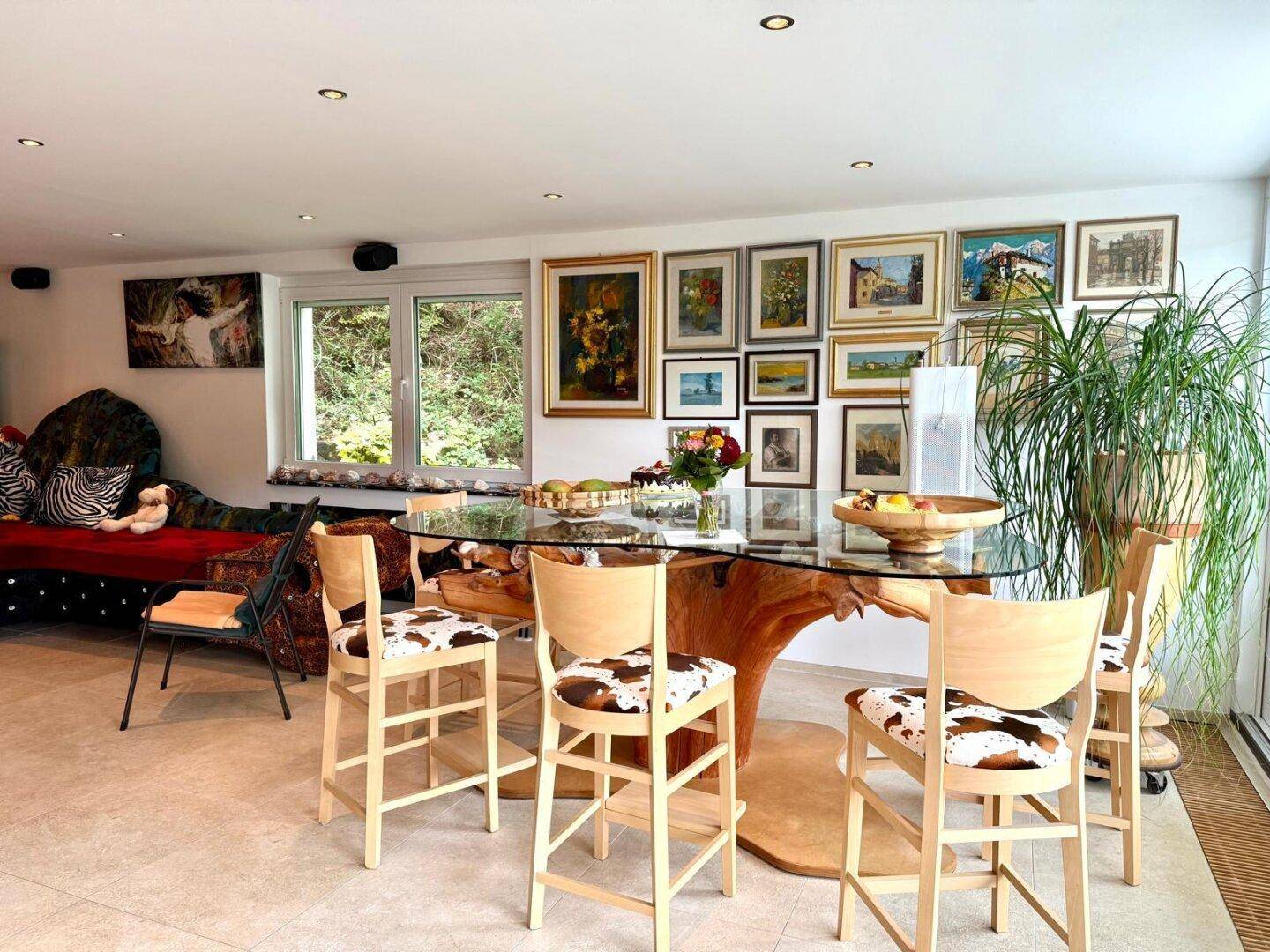 Essbereich mit großem Glastisch, Holzstühlen und vielen Bildern an der Wand.