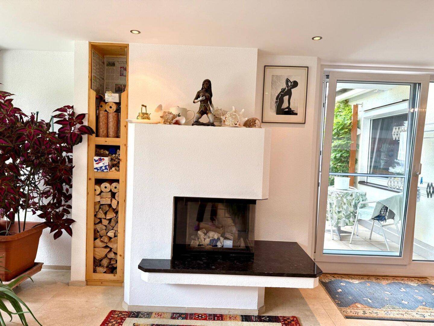 Wohnzimmer mit modernem Kamin, Holzregal und Zugang zur Terrasse.