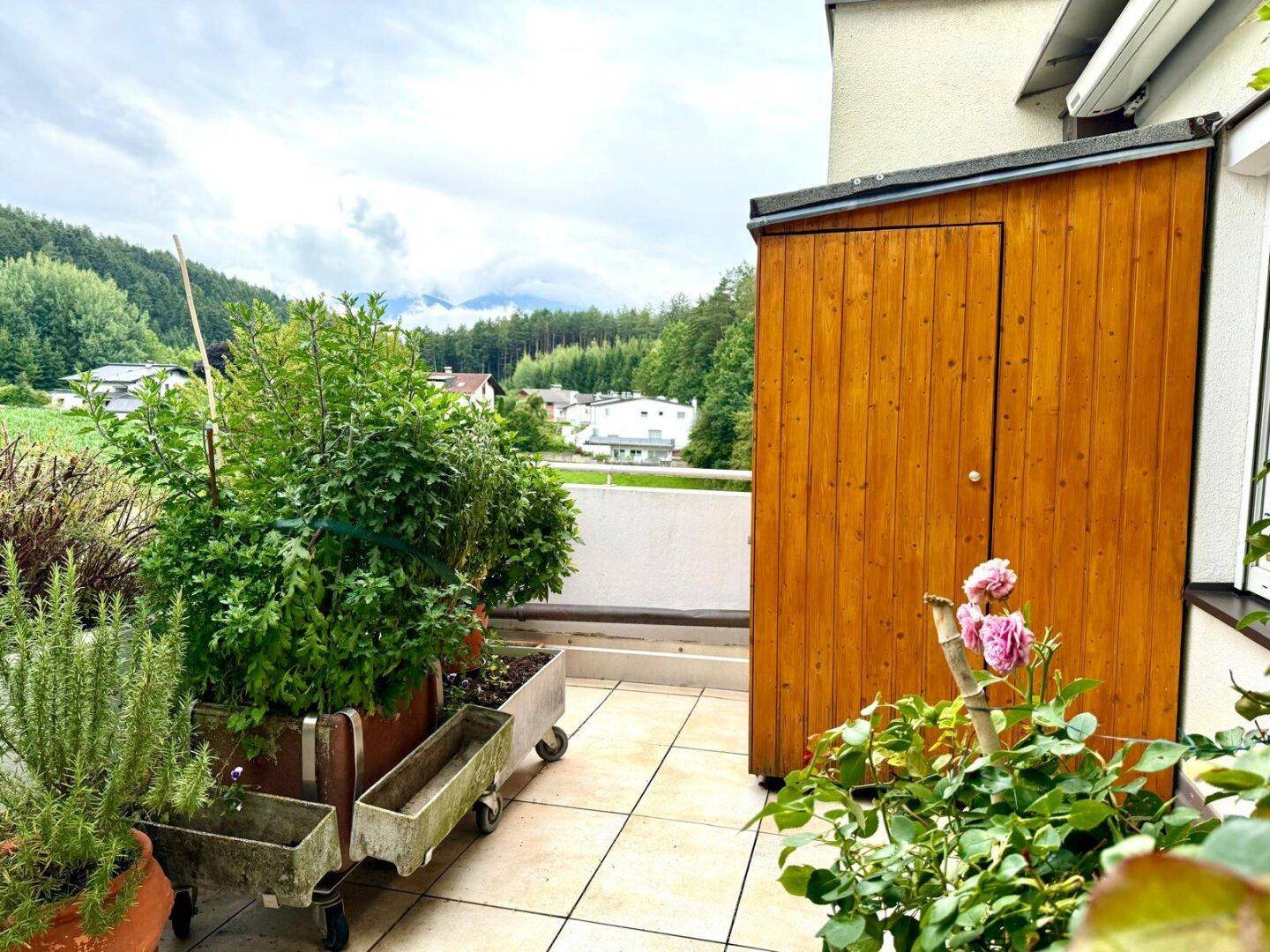 Terrasse mit Holzschrank, Pflanzen und Blick auf die umliegende Landschaft.