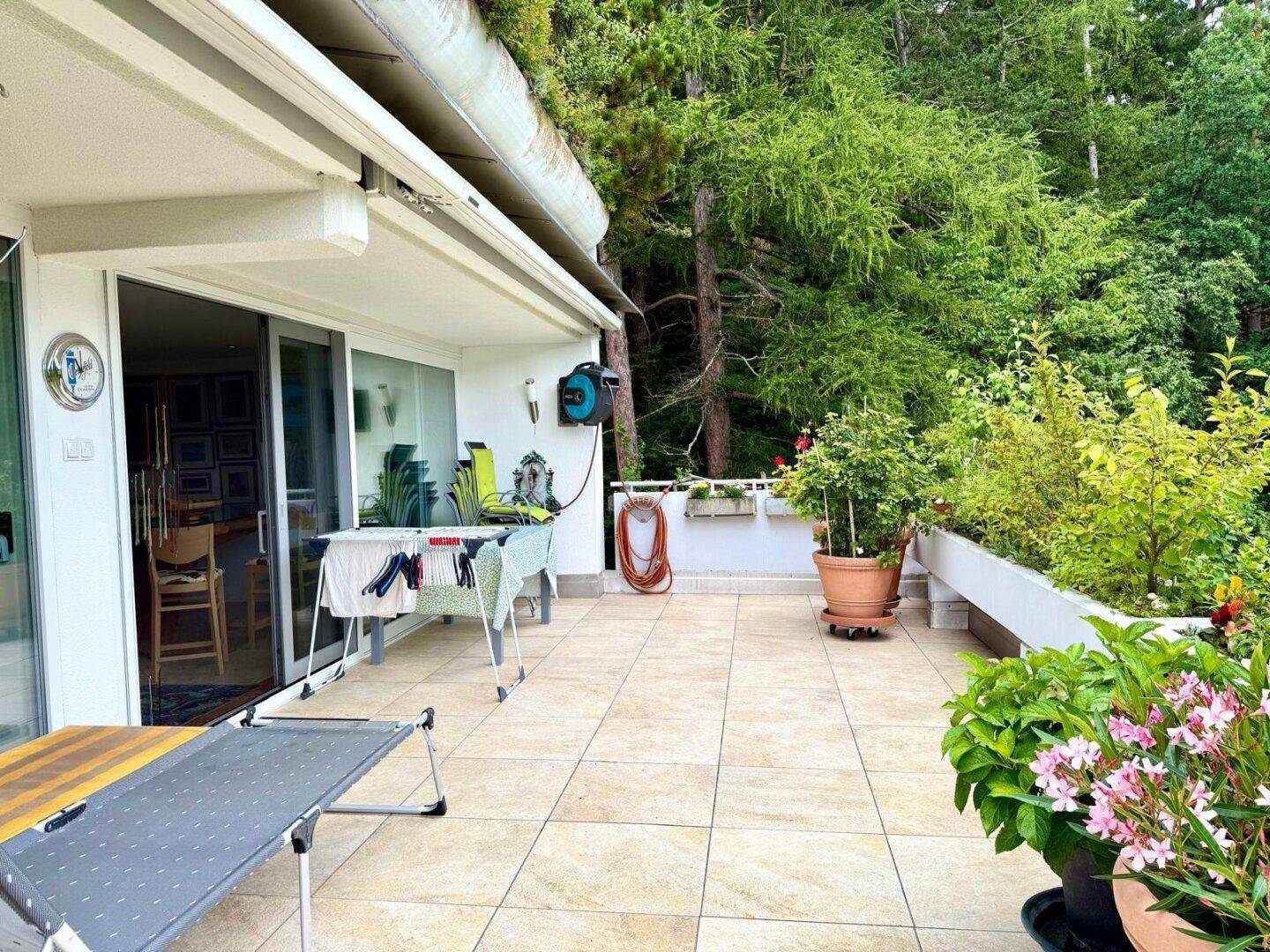 Große geflieste Terrasse mit Gartenmöbeln, Pflanzen und Blick auf die grüne Umgebung.