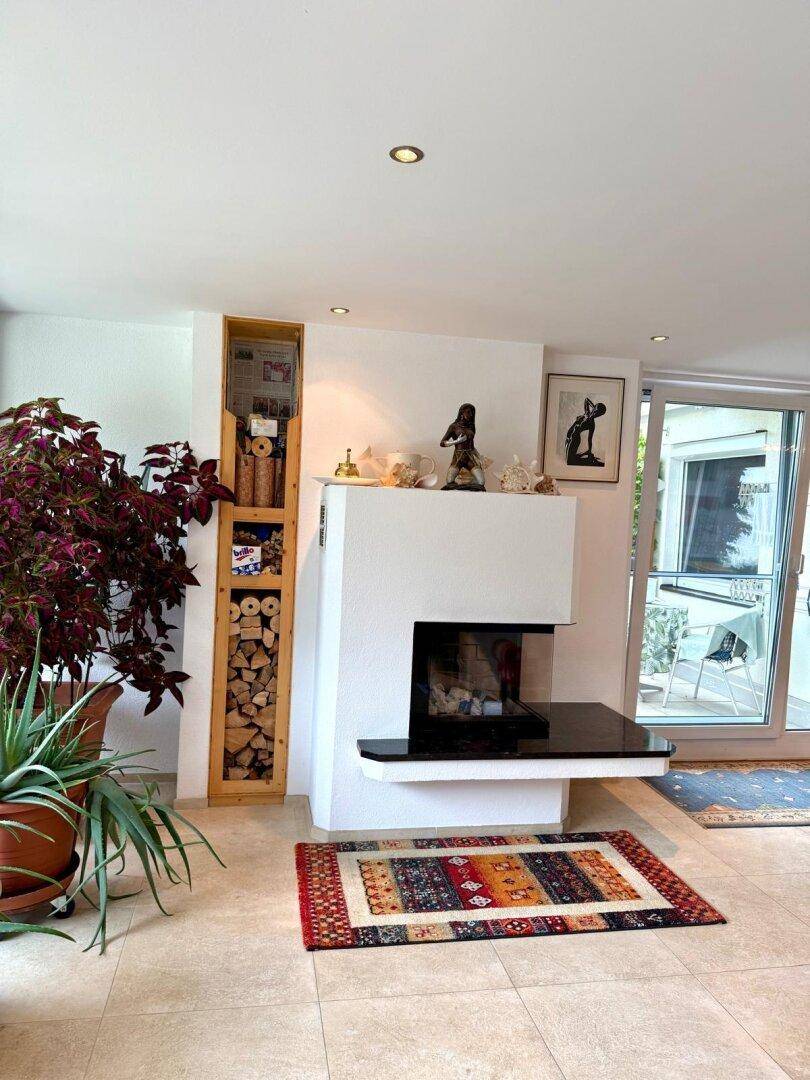 Wohnzimmer mit modernem Kamin, Holzregal und Zugang zu einem Außenbereich.