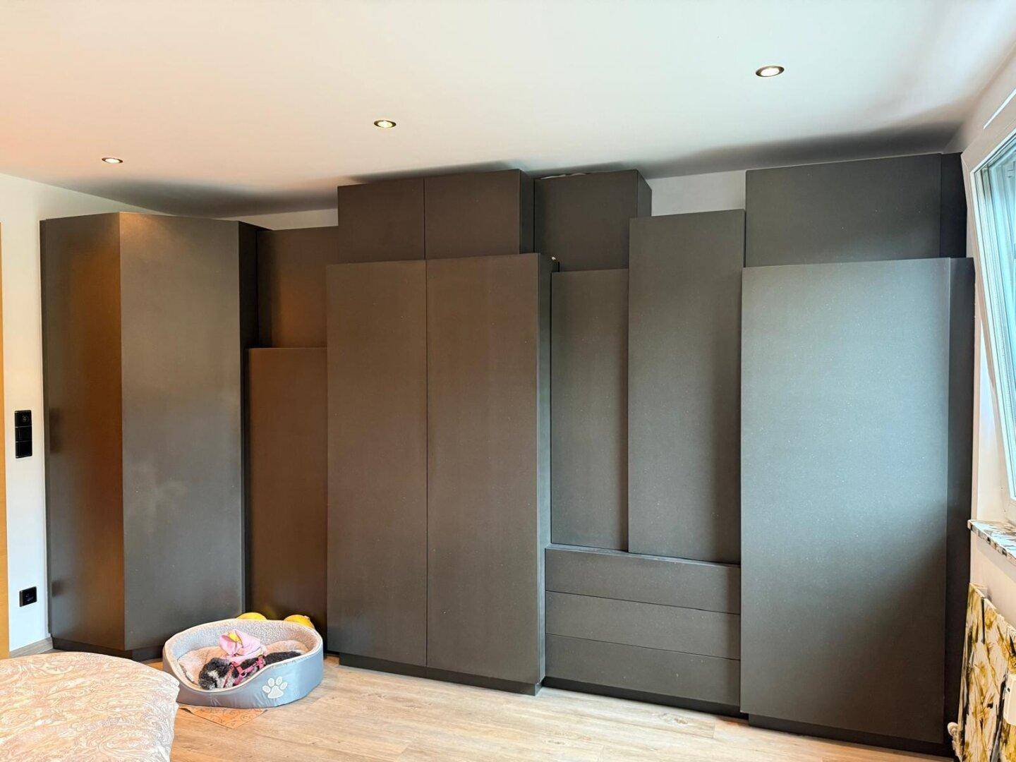 Schlafzimmer mit großem Einbauschrank in dunklem Grau und hellem Holzboden.