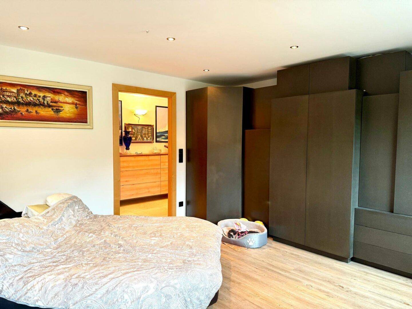 Schlafzimmer mit großem Bett, Einbauschränken und Zugang zu einem weiteren Raum.