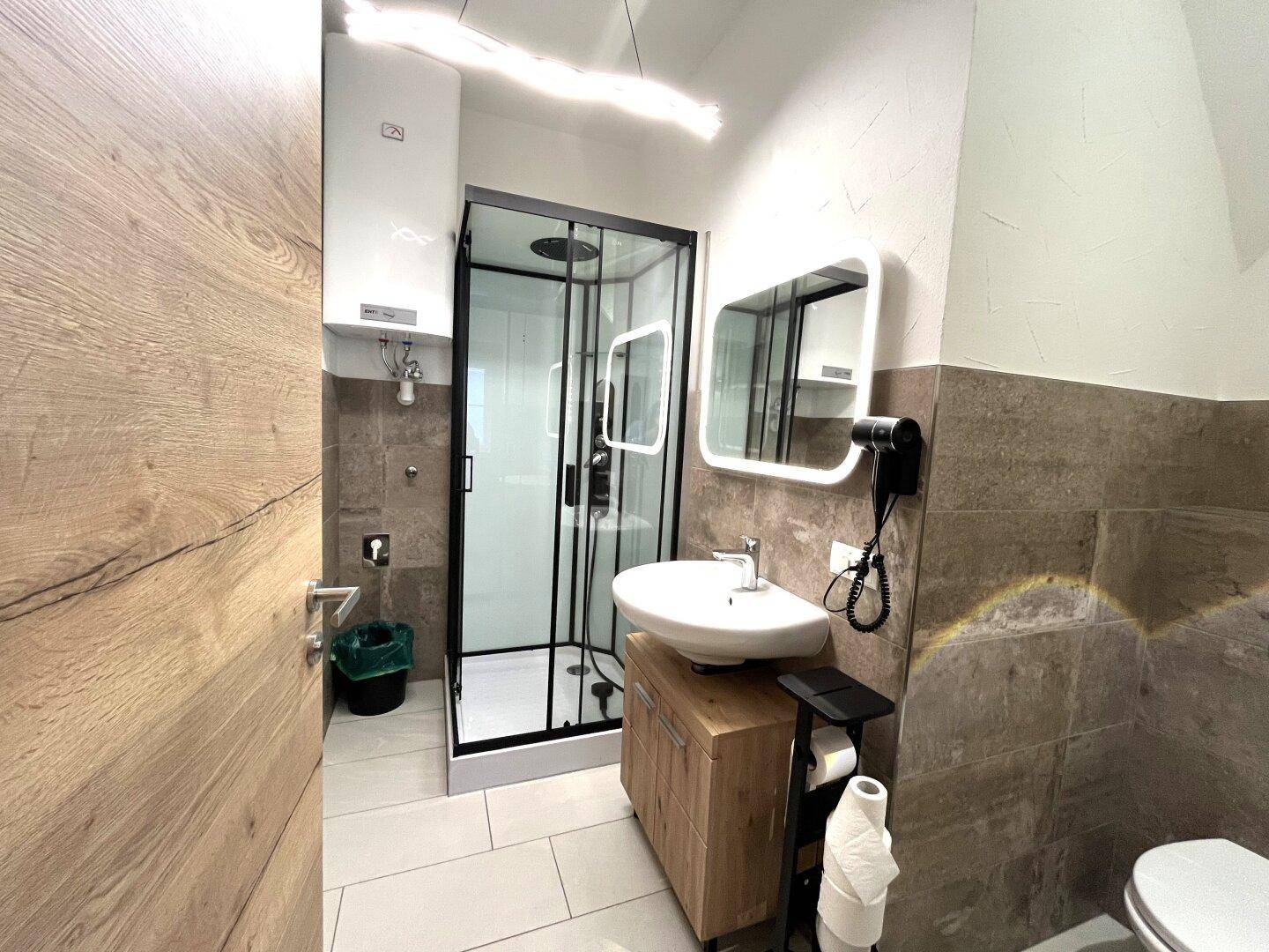Modernes Badezimmer mit Duschkabine, Waschbecken und Wandfliesen in Erdtönen.