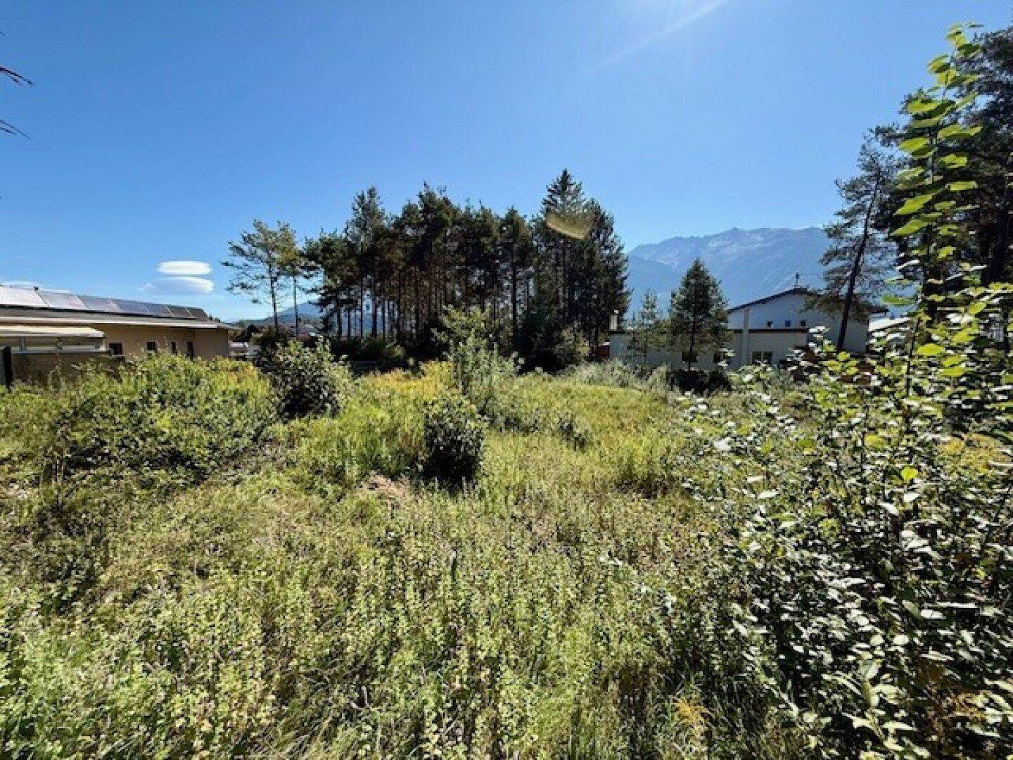 Sonniges Grundstück mit Blick auf die Berge und angrenzende Häuser mit Solaranlagen.