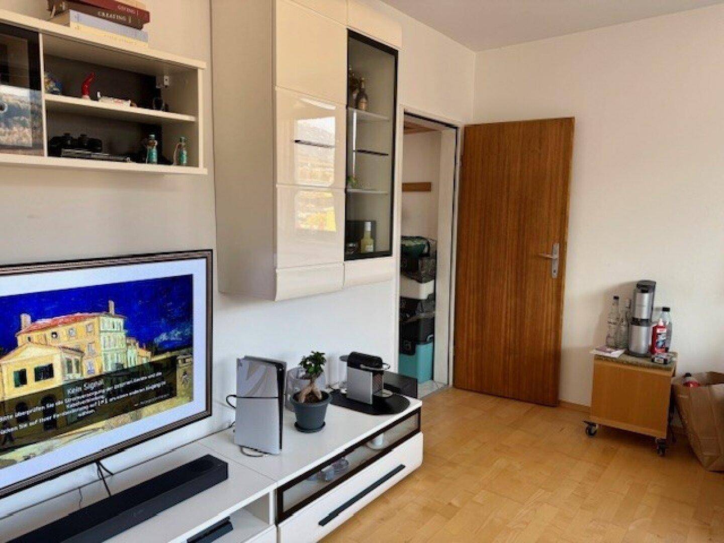 Heller Wohnbereich mit Fernseher, modernen Möbeln und Zugang zu einem weiteren Raum.