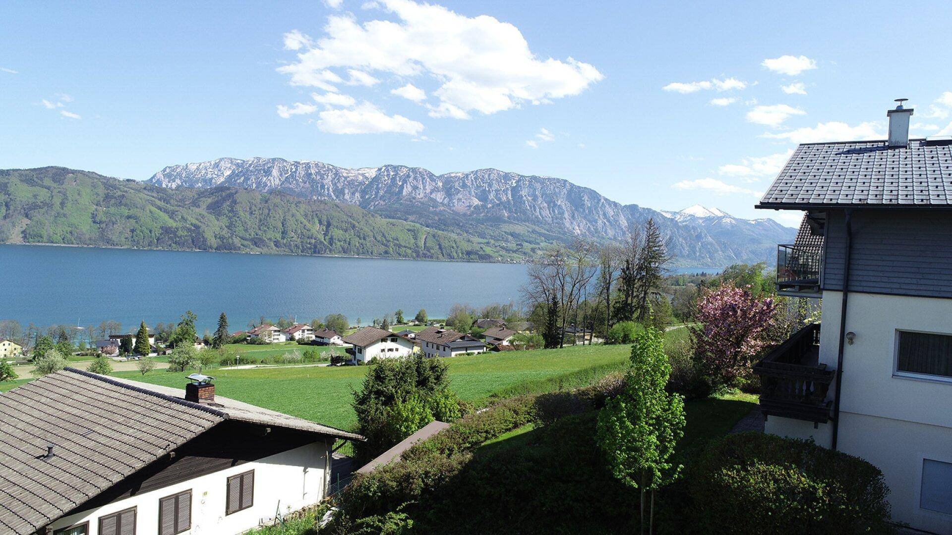 Panoramablick auf den See und schneebedeckte Berge von einer erhöhten Position mit umliegenden Häusern.