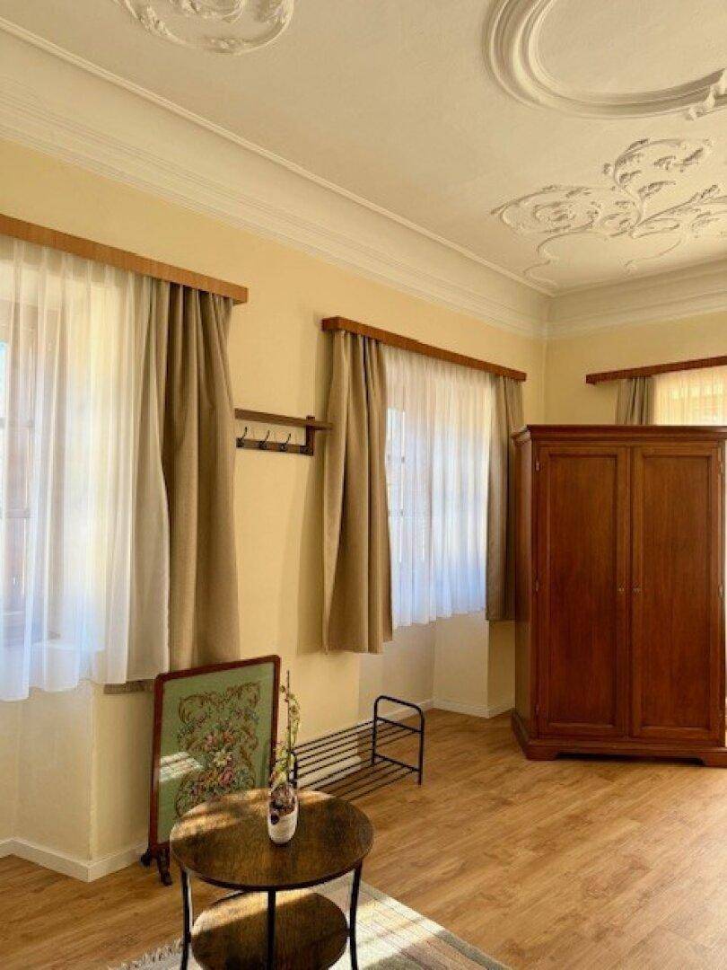 Gemütliches Zimmer mit Holzboden, klassischem Kleiderschrank und dekorativer Stuckdecke.