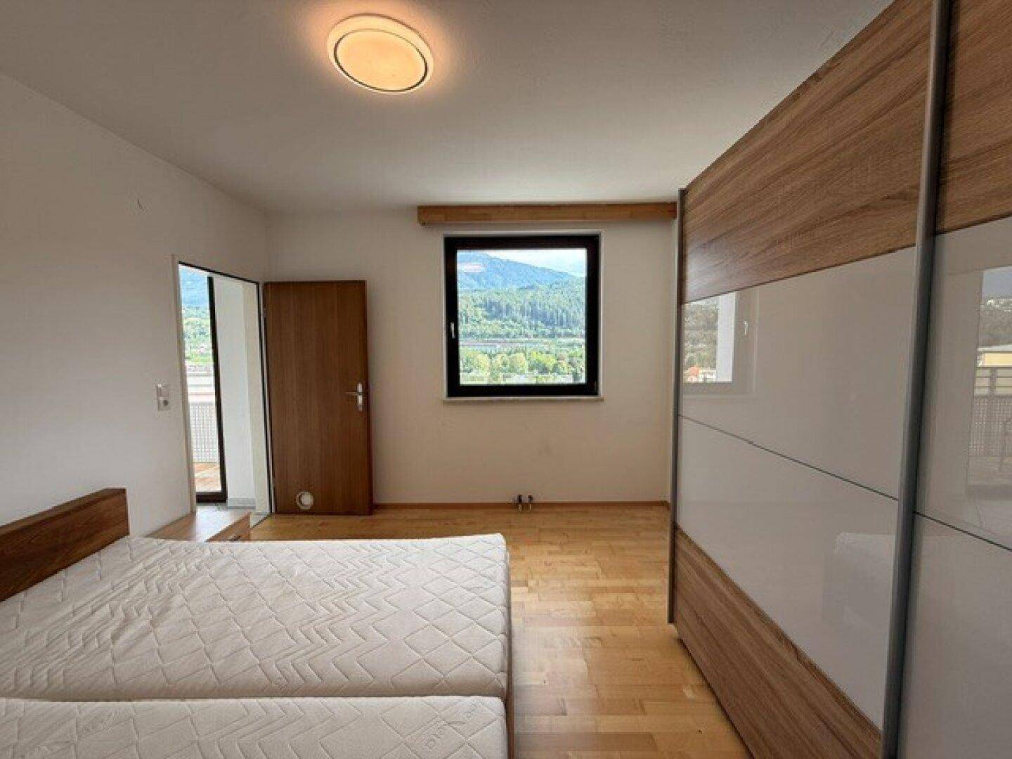 Helles Schlafzimmer mit Parkettboden, Fensterblick und direktem Zugang zum Balkon.