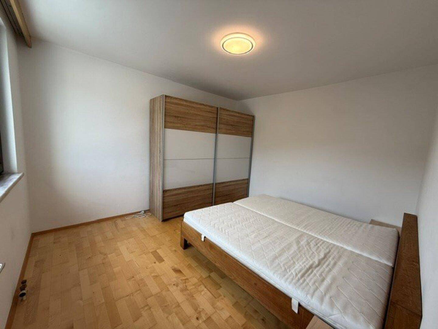Schlafzimmer mit Doppelbett und großem Schiebetürenschrank, ausgestattet mit Parkettboden.