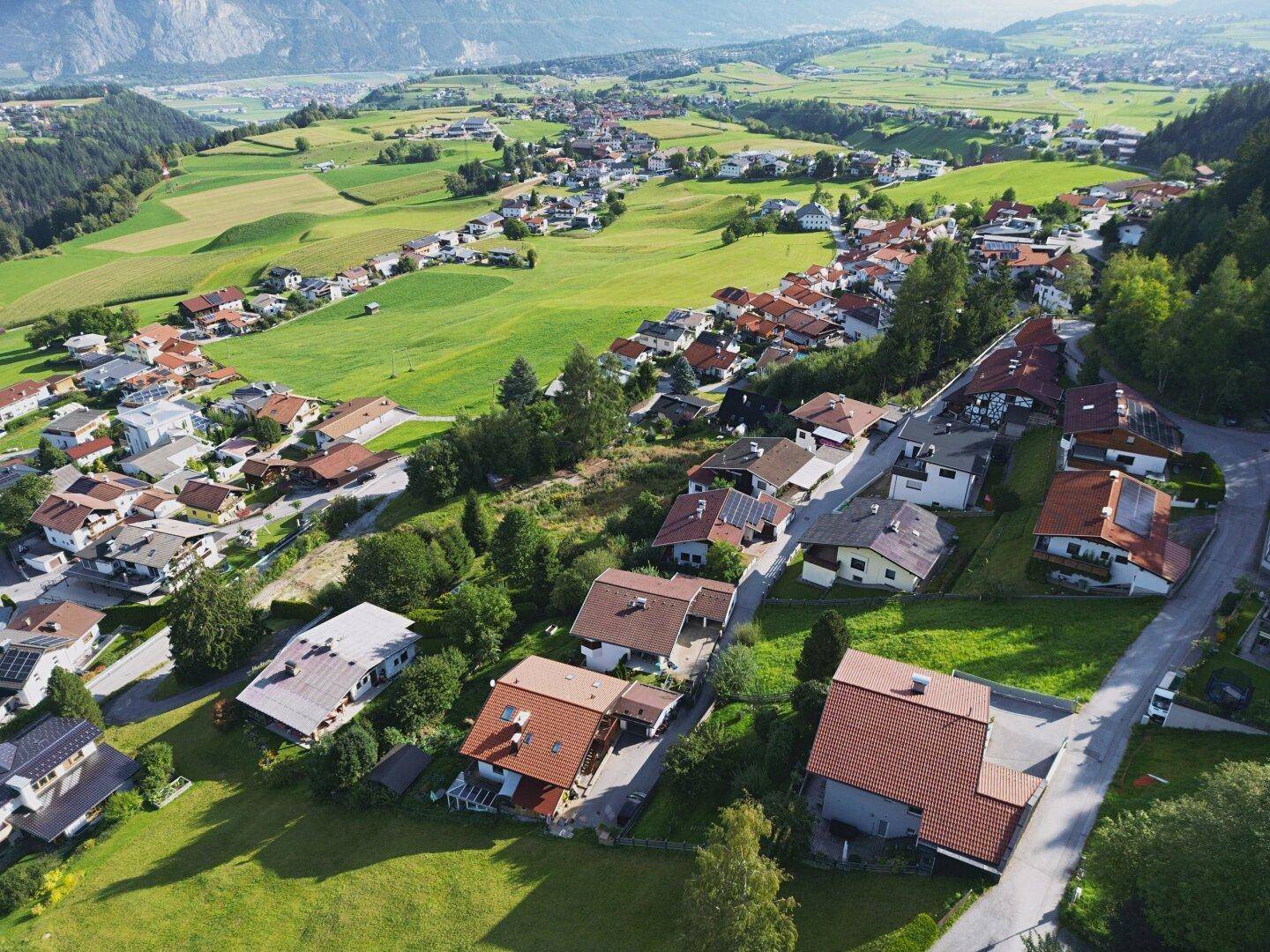 Panoramablick auf die ländliche Siedlung mit grünen Feldern und majestätischen Bergen im Hintergrund.
