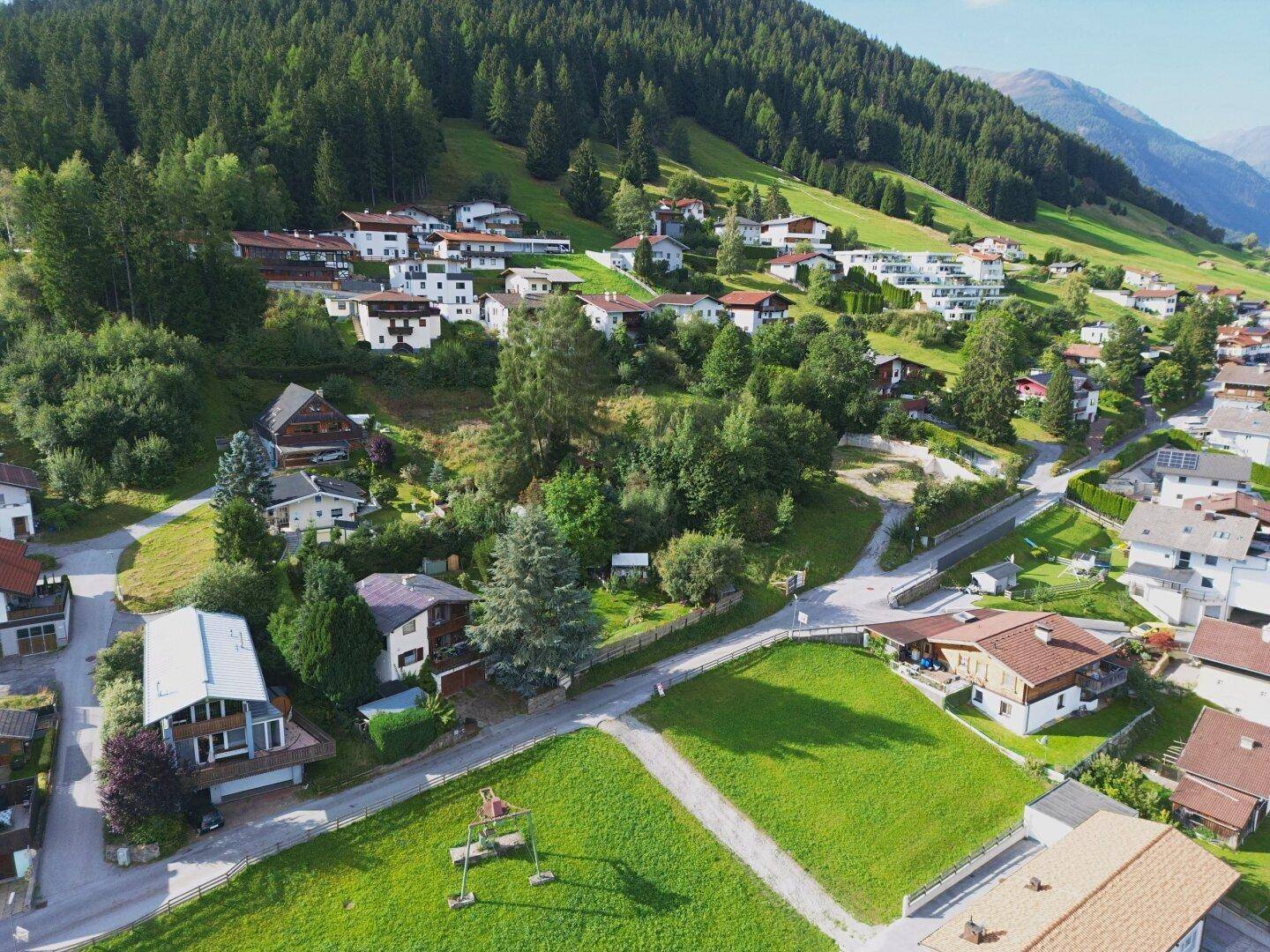 Malerische Luftaufnahme eines Dorfes in einem Tal, umgeben von bewaldeten Bergen und grünen Hängen.