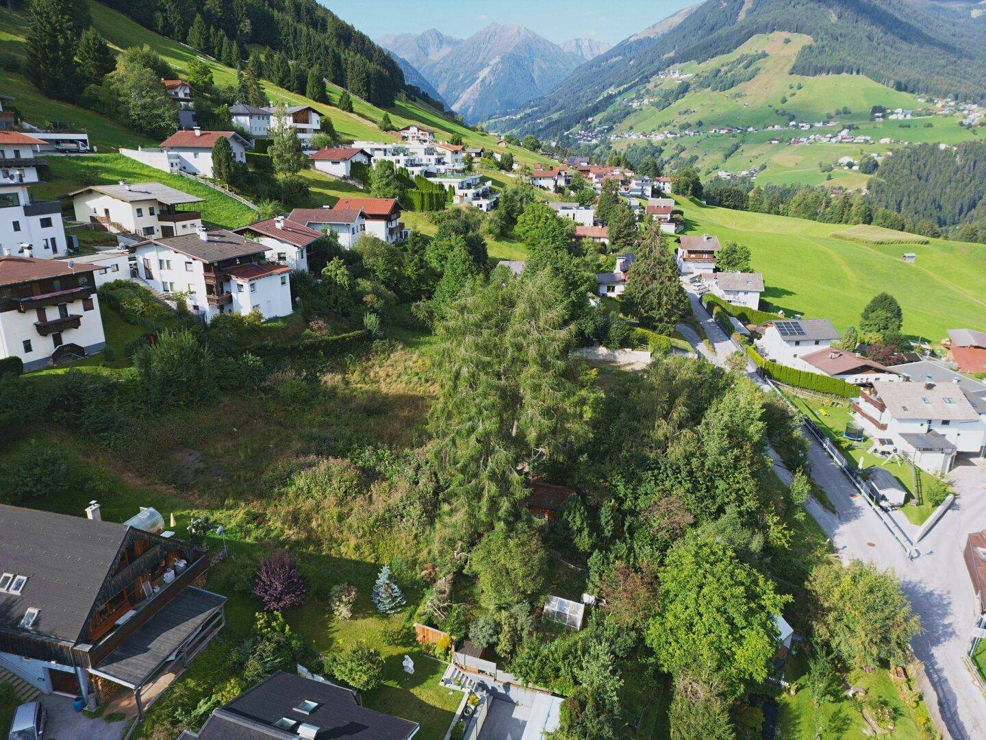 Weitläufige Ansicht des Tals mit verstreuten Häusern und imposanten Bergketten im Hintergrund.