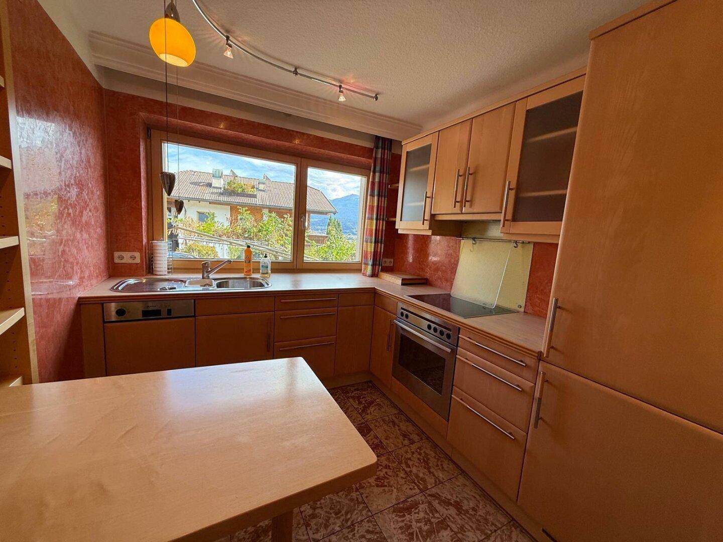Funktionale Küche mit Holzschränken, Fliesenboden und Fensterblick auf die Umgebung.