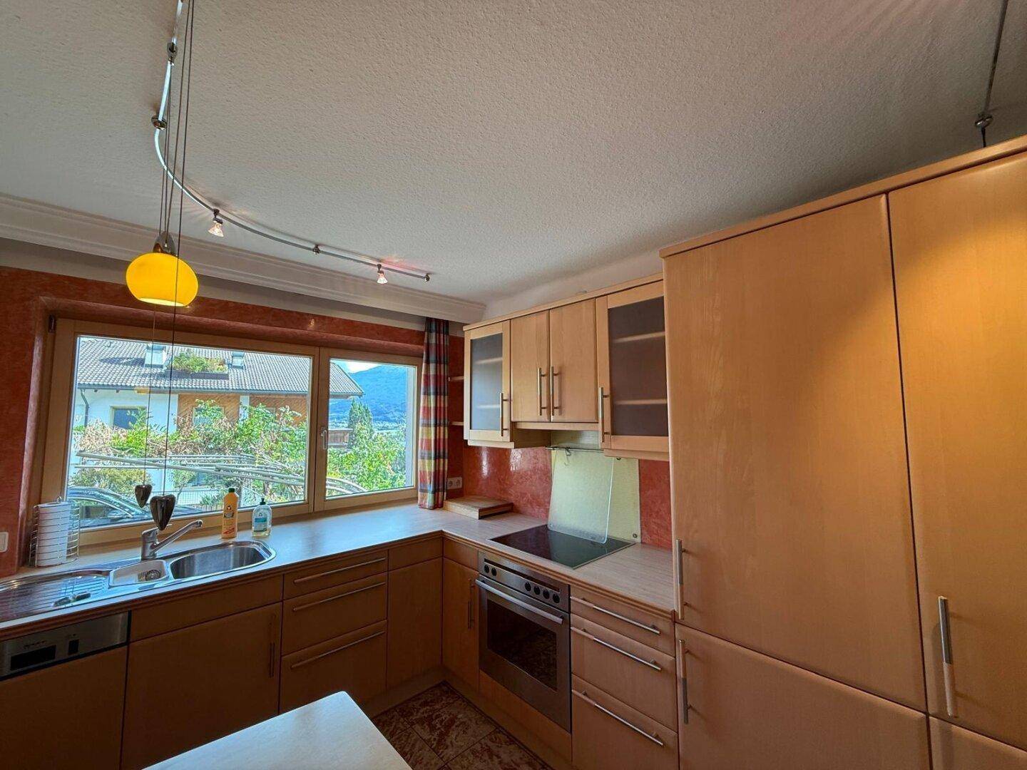 Helle Küche mit Holzfronten, integrierten Geräten und Blick auf die umliegende Landschaft.