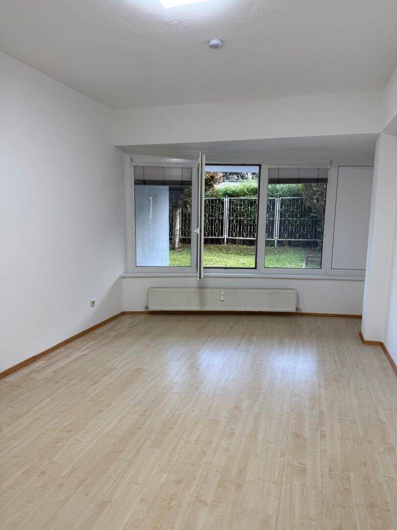 Heller Raum mit Laminatboden und großen Fenstern, die einen Blick ins Grüne bieten.