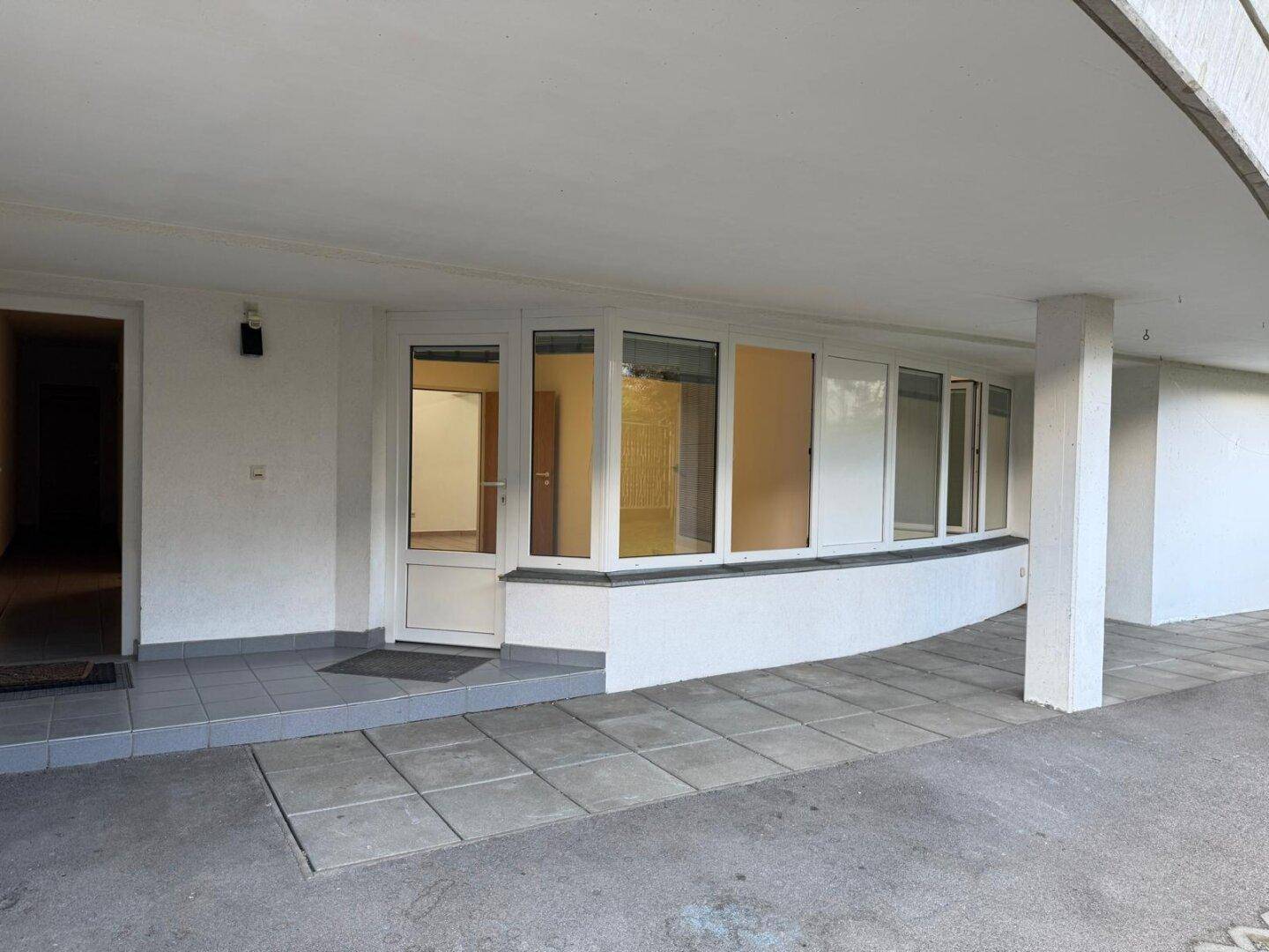 Eingangsbereich des Gebäudes mit großer Fensterfront und gepflastertem Zugangsbereich.