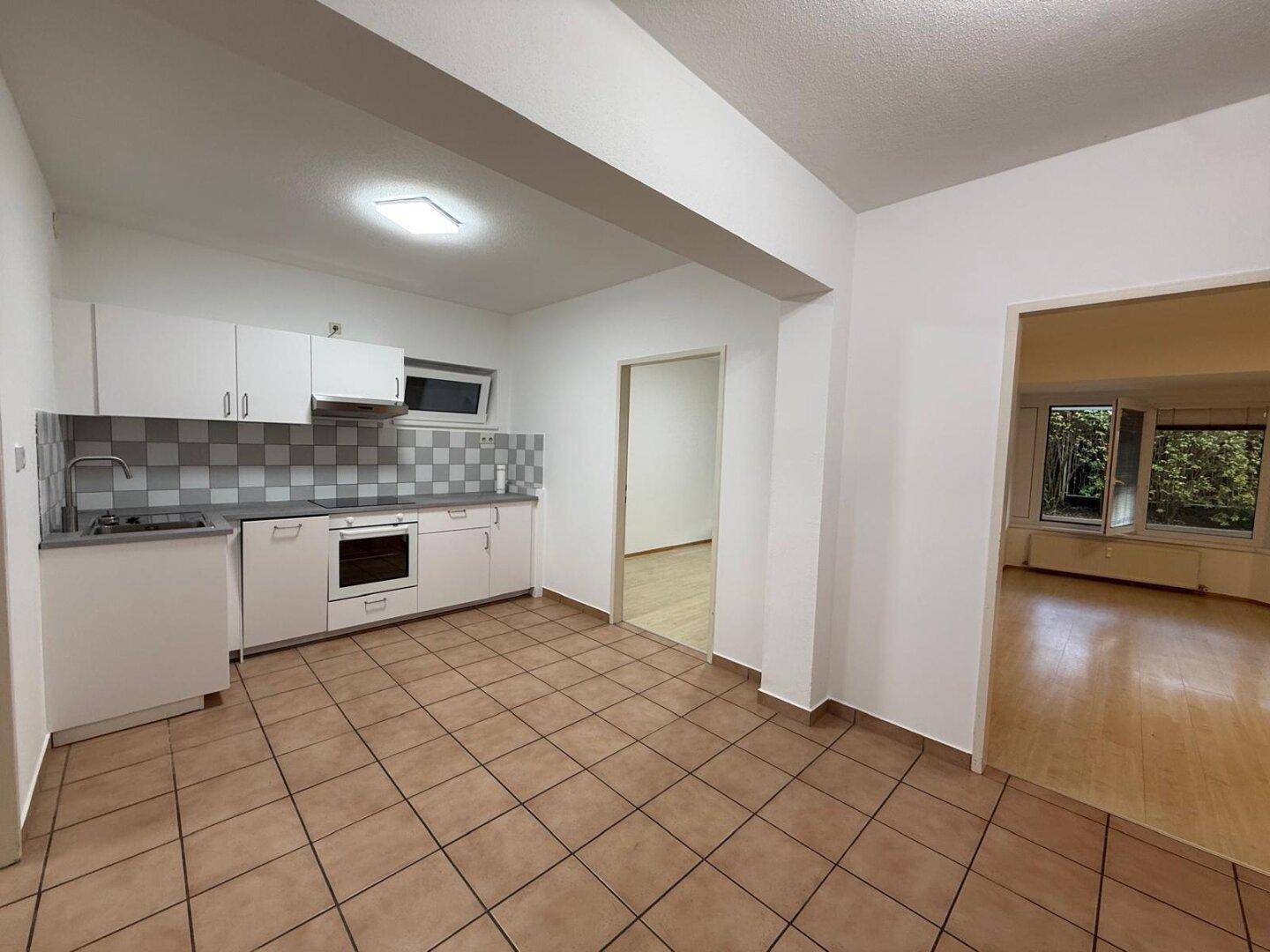 Funktionale Küche mit weißen Schränken, Fliesenboden und Blick in den angrenzenden Wohnbereich.
