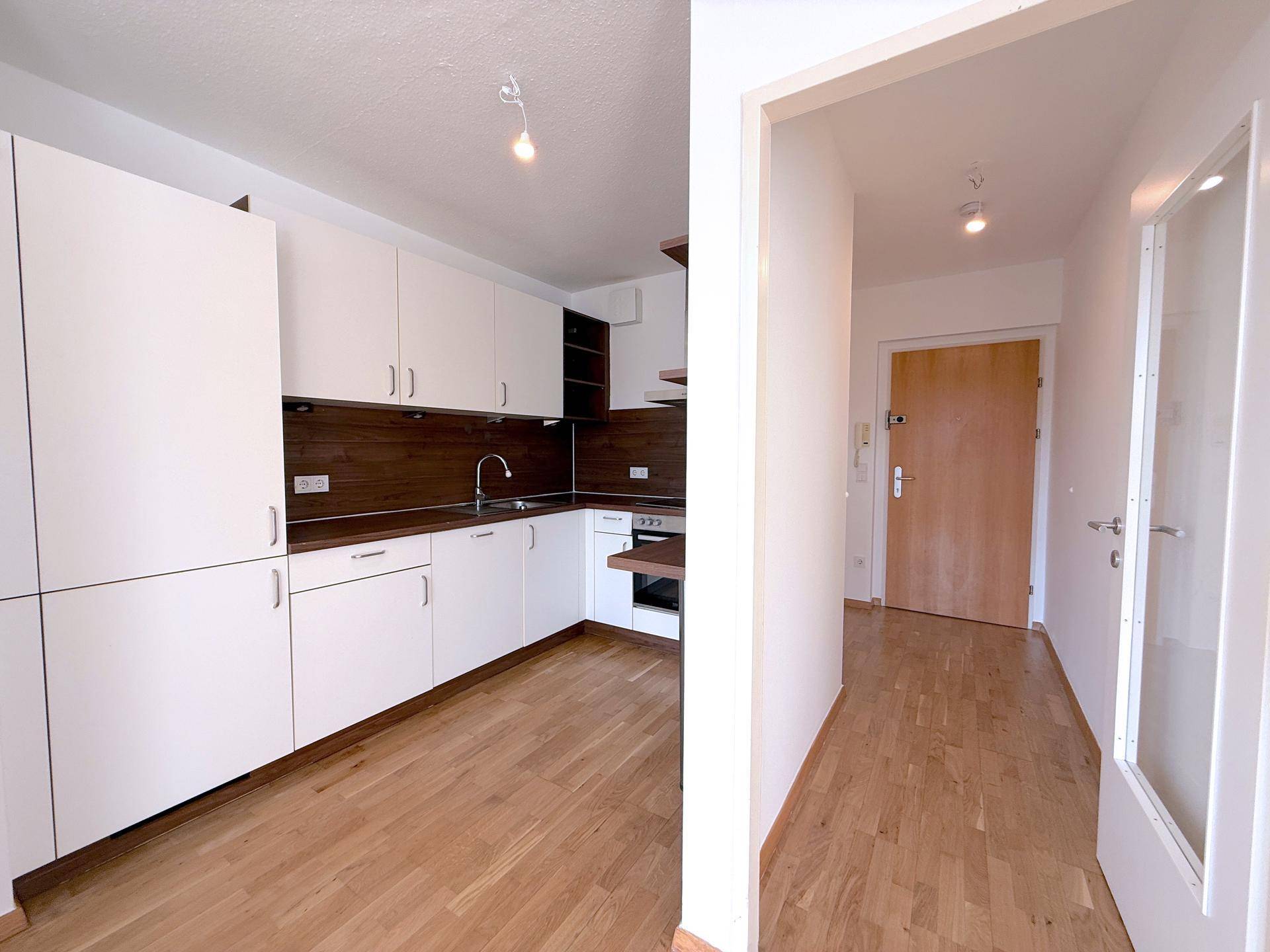 Funktionale Einbauküche mit weißen Schränken, Holz-Arbeitsplatte und Parkettboden im Eingangsbereich.