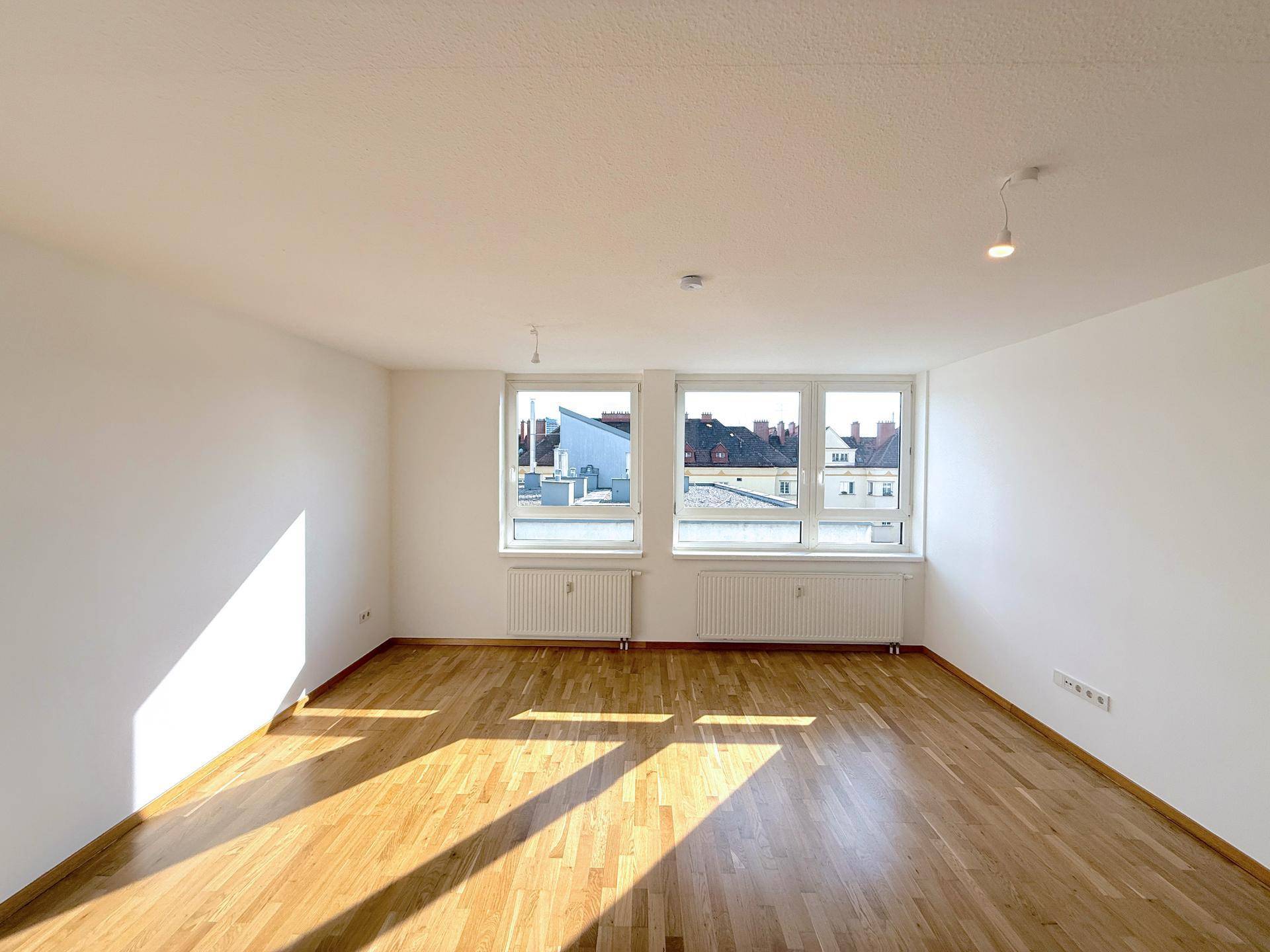 Geräumiges, helles Wohnzimmer mit Holzboden und großen Fenstern, die eine weite Aussicht bieten.