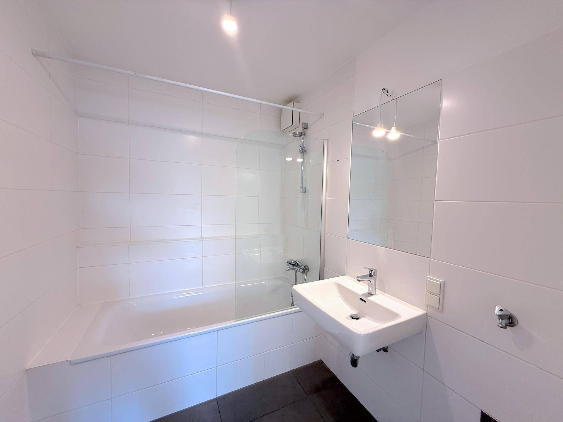 Modernes Badezimmer mit weißen Fliesen, Badewanne mit Duschabtrennung und einem Waschbecken.