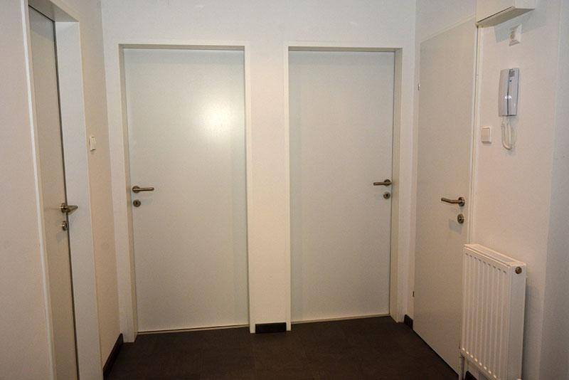 Heller Flur mit dunklem Boden und mehreren Türen, ausgestattet mit Heizkörper und Gegensprechanlage.