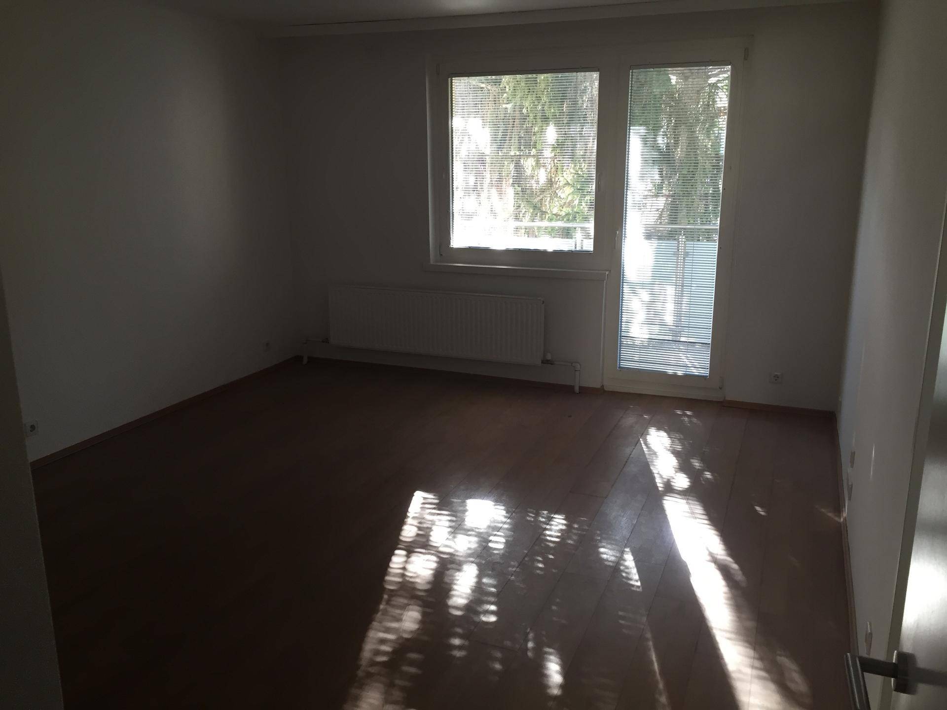 Lichtdurchfluteter Raum mit Laminatboden und großem Fenster, das viel Sonnenlicht hereinlässt.