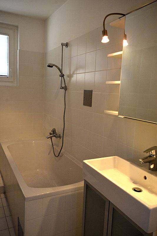 Modernes Badezimmer mit Badewanne, Duscharmatur und Waschbecken, ausgestattet mit Spiegel und Beleuchtung.