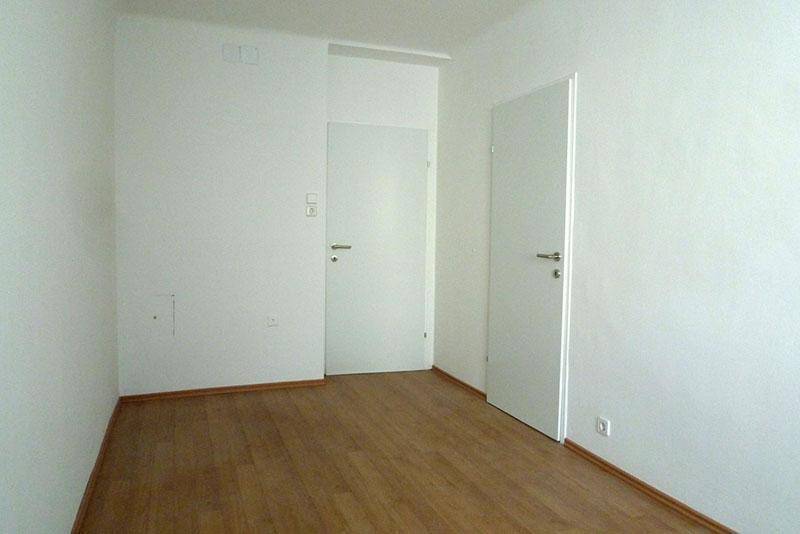Leerer Raum mit hellem Laminatboden und weißen Wänden, bereit zur individuellen Gestaltung.