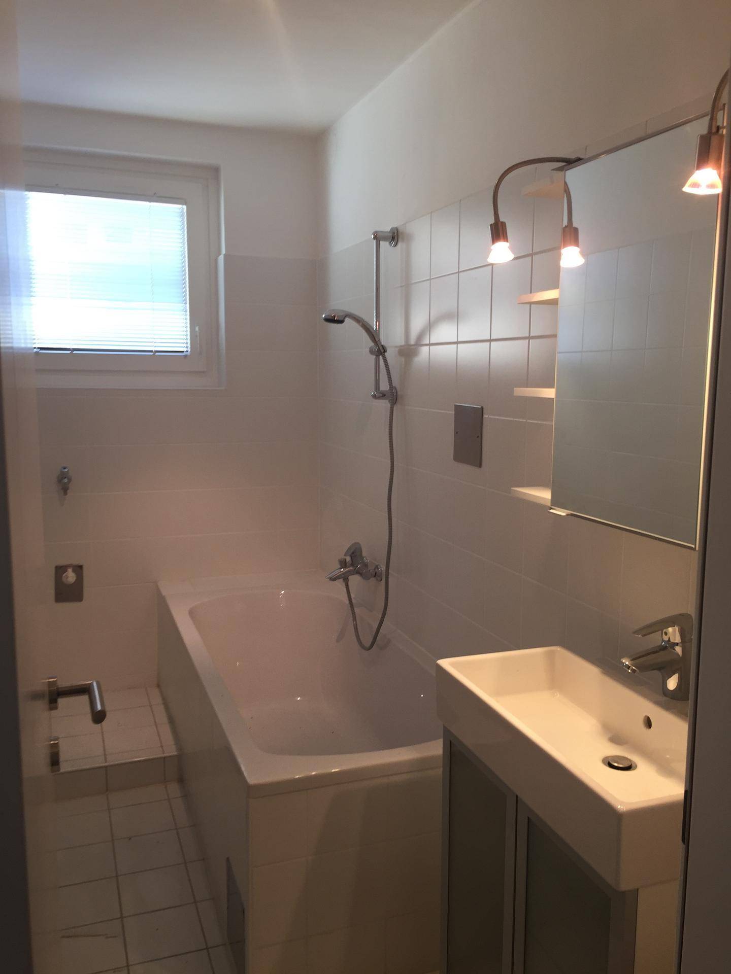 Helles Badezimmer mit Badewanne, Duschfunktion, Waschbecken und Fenster für natürliche Belüftung.