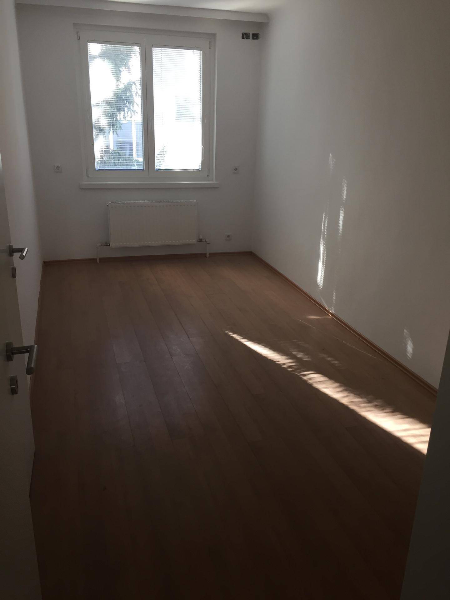Leerer Raum mit Laminatboden und großem Fenster, das viel Tageslicht hereinlässt.