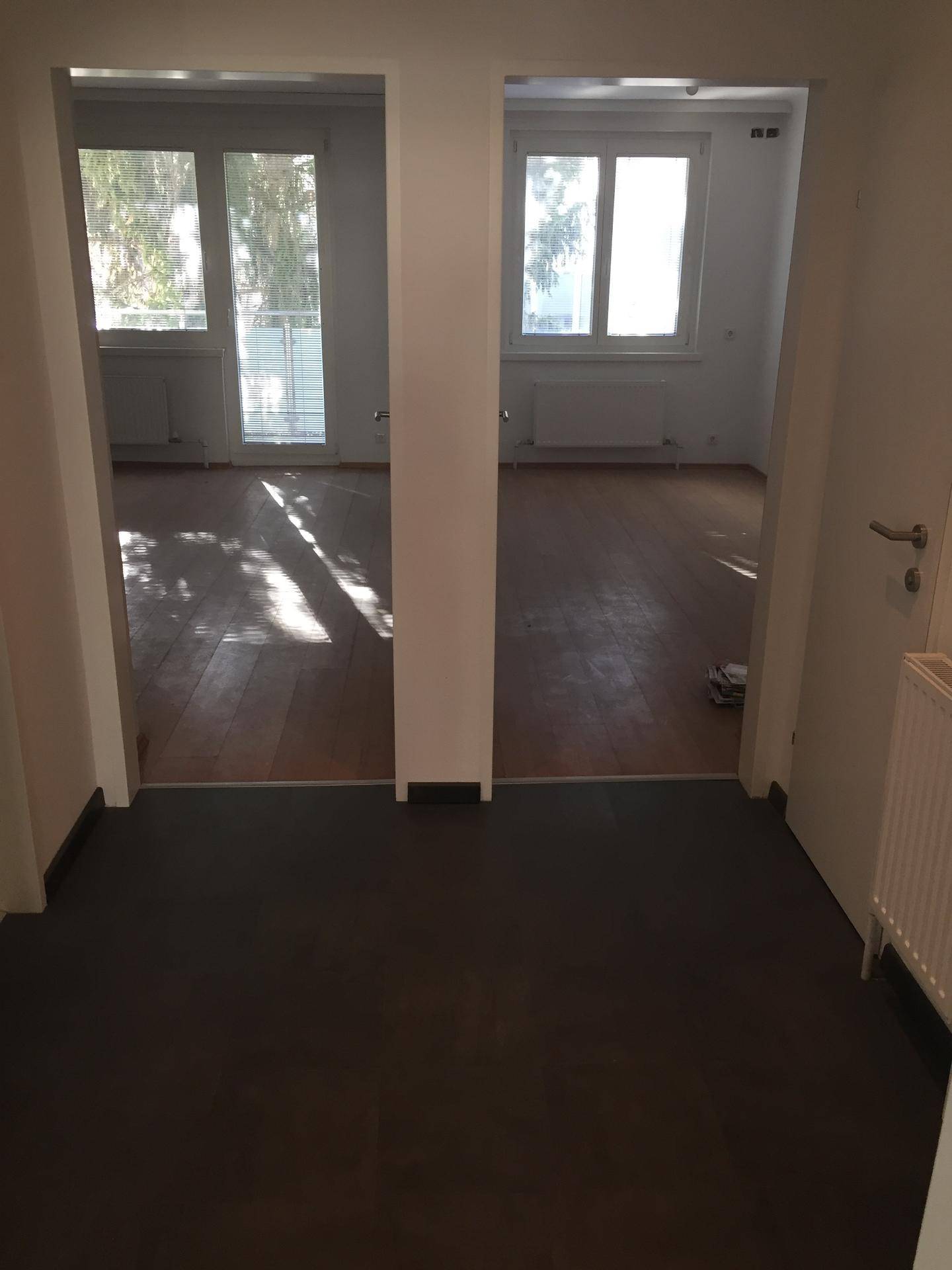 Flur mit dunklem Boden, der zu zwei hellen Räumen mit Laminatboden führt.