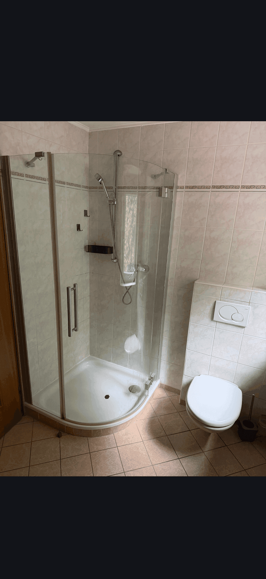 Badezimmer mit Eckduschkabine, wandhängendem WC und hellen Fliesen an Wänden und Boden.