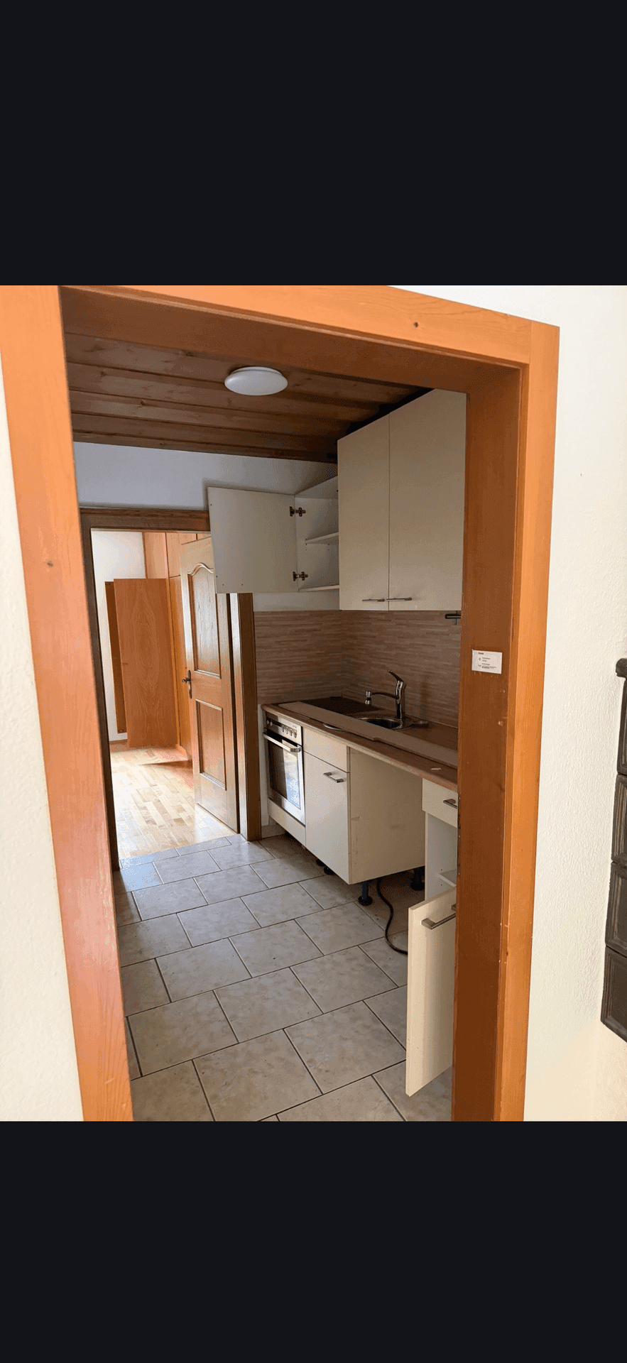 Kleine Küchenzeile in einem schmalen Flur mit hellen Fliesen und Holzdecke.