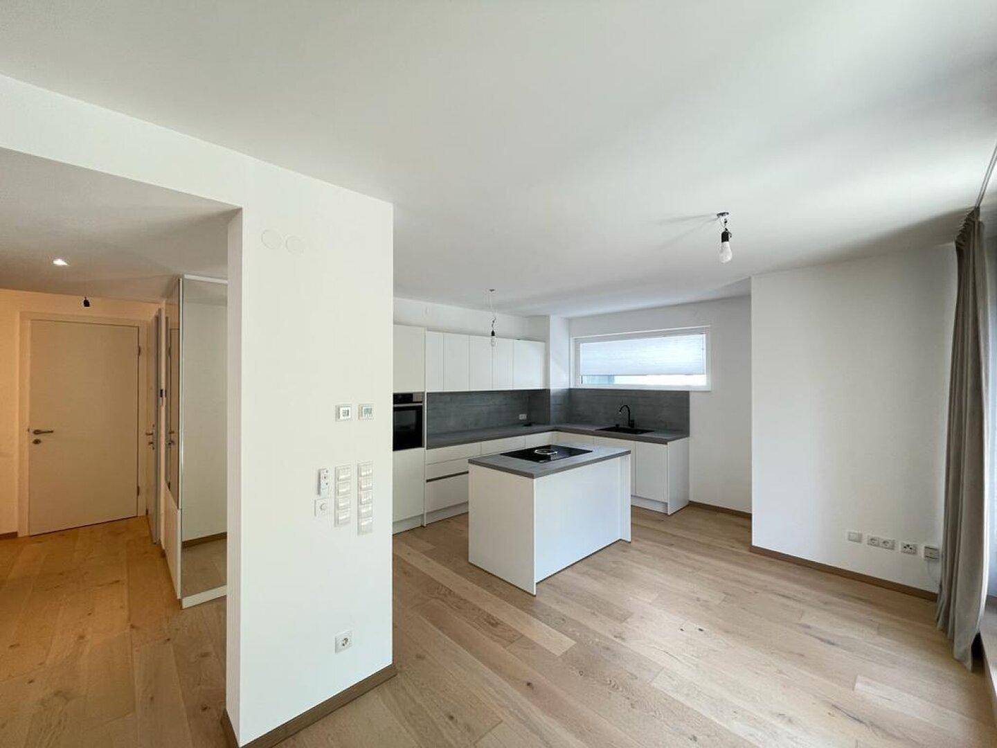 Moderne, offene Küche mit Kochinsel, hellen Schränken und Holzboden, verbunden mit dem Wohnbereich.