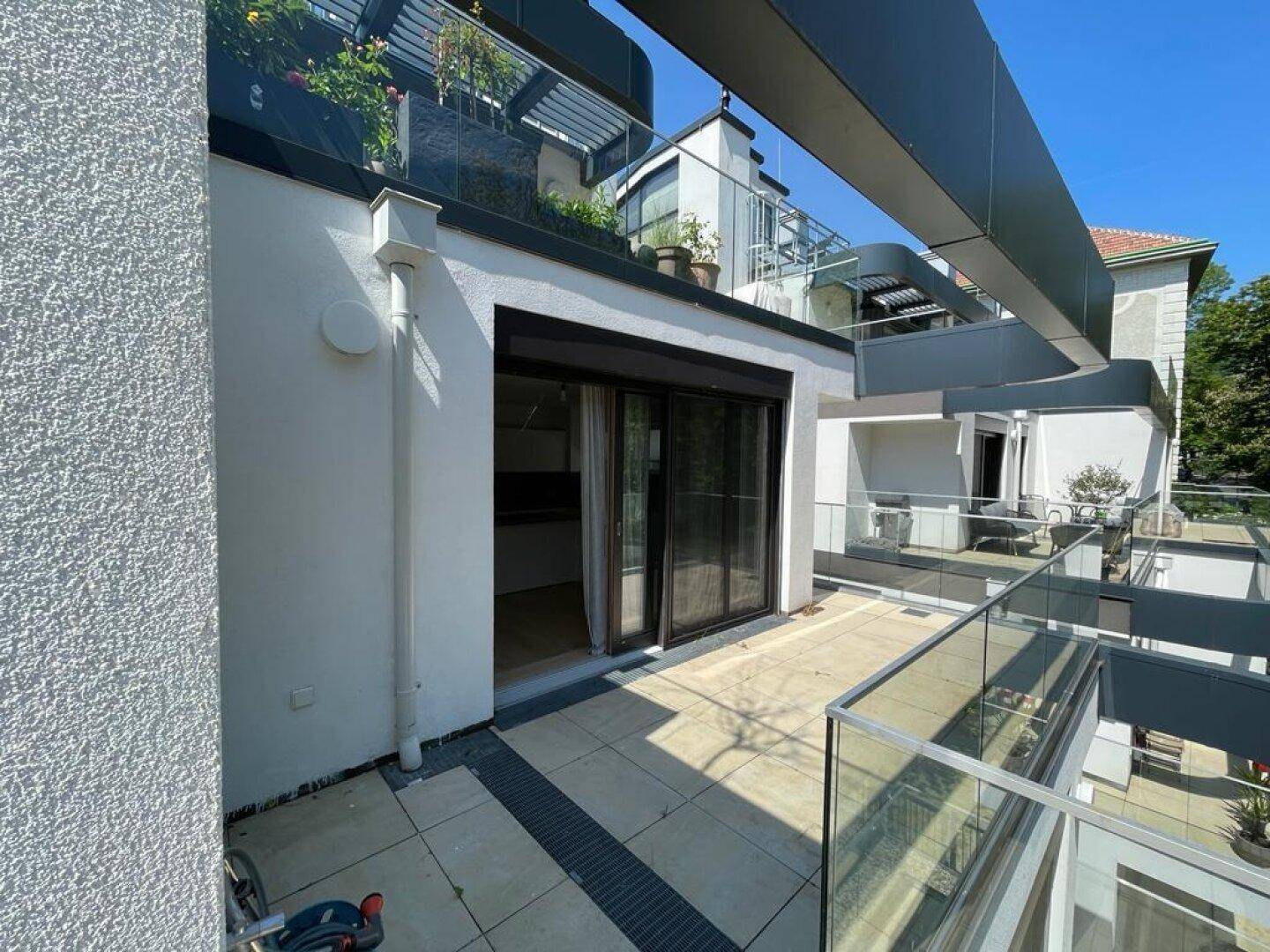 Sonniger Terrassenbereich mit Schiebetürzugang zu einem Innenraum und Glasgeländer.