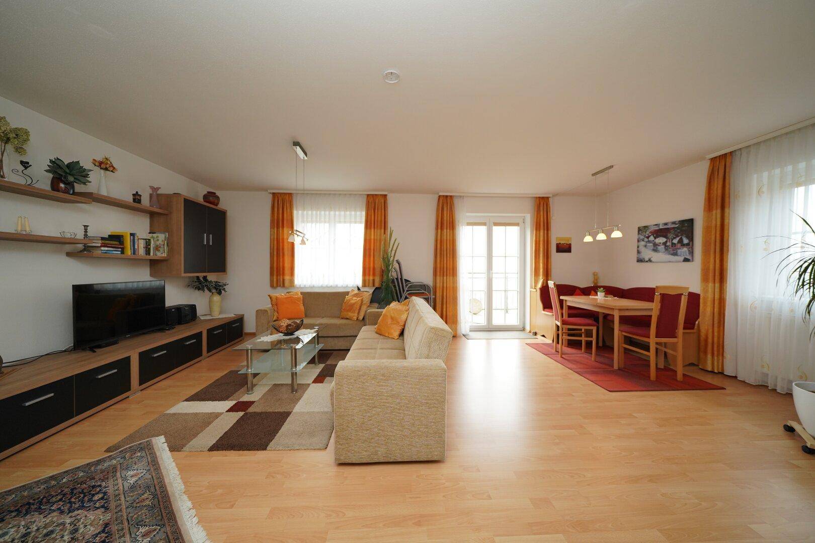 Geräumiger Wohn-Essbereich mit hellem Laminatboden, gemütlicher Sitzecke und Zugang zum Balkon.