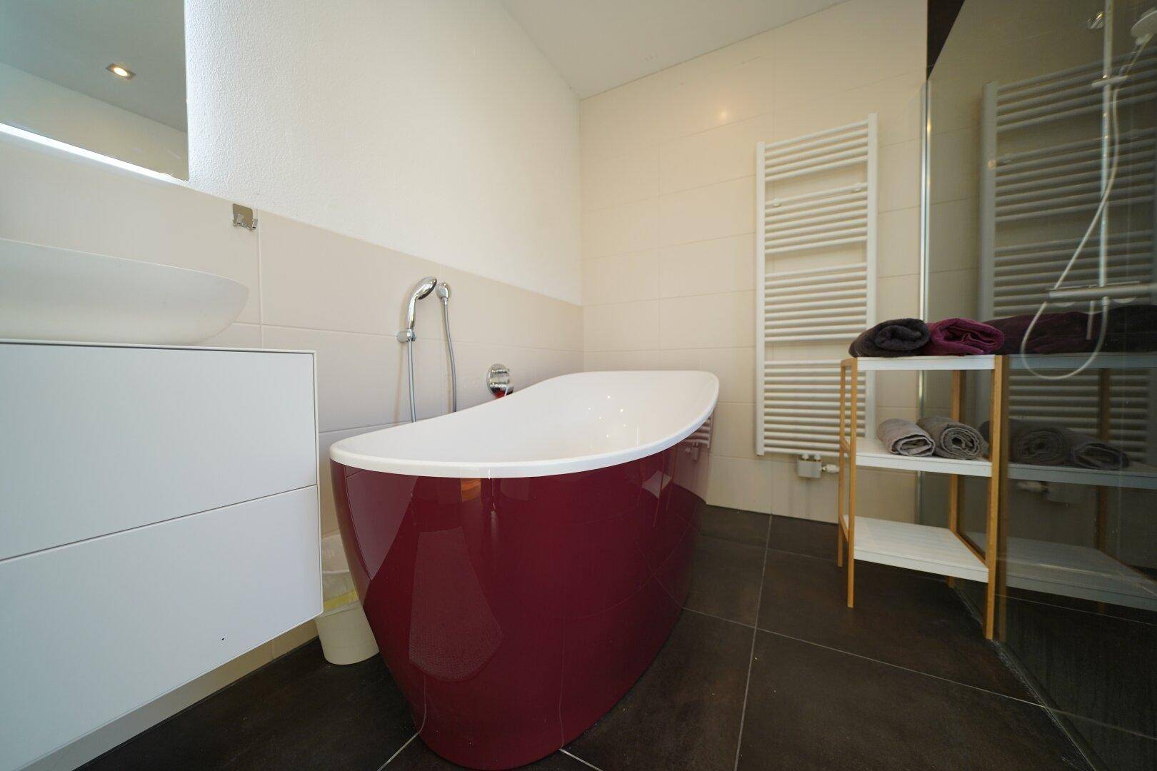 Modernes Badezimmer mit freistehender roter Badewanne und beheiztem Handtuchhalter.