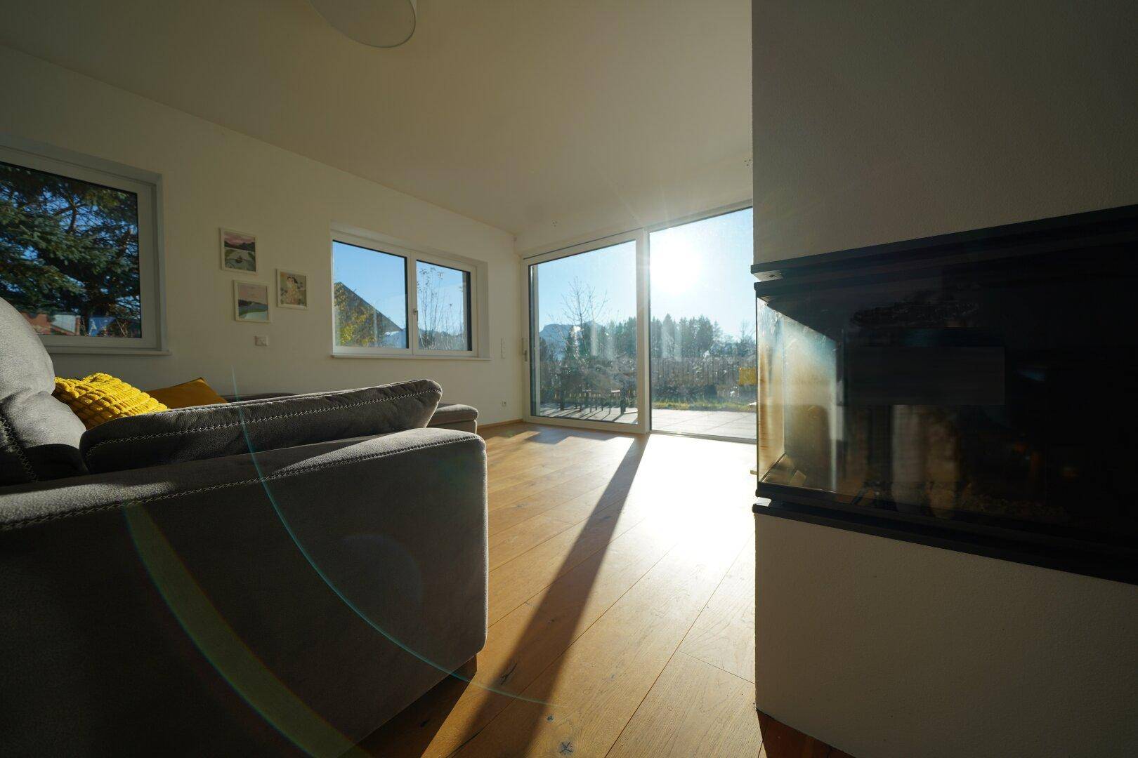 Helles Wohnzimmer mit Kamin, Holzboden und großem Schiebefenster zur Terrasse.