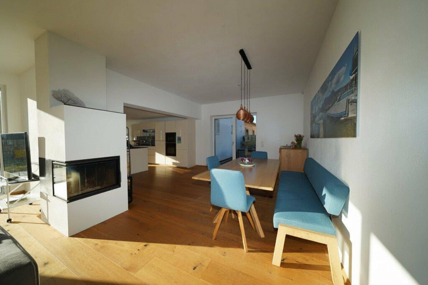 Offener Essbereich mit Holzboden, modernem Kamin und Blick in die Küche.