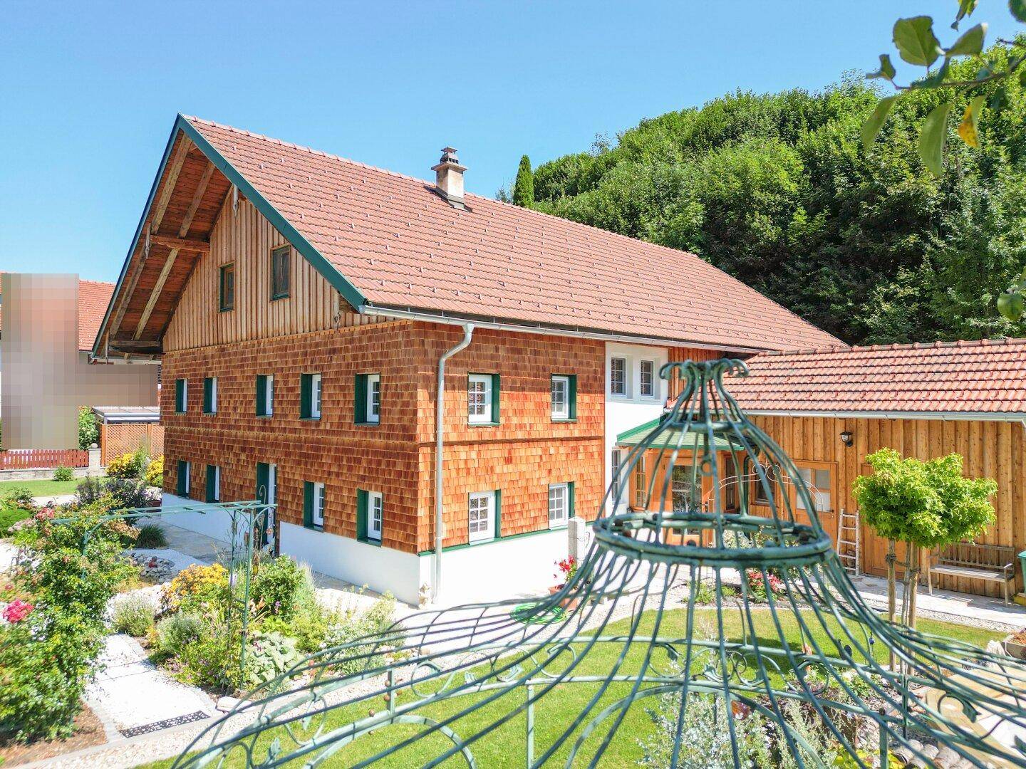 Traditionelles Holzhaus mit Ziegeldach und gepflegtem Garten in ländlicher Umgebung.