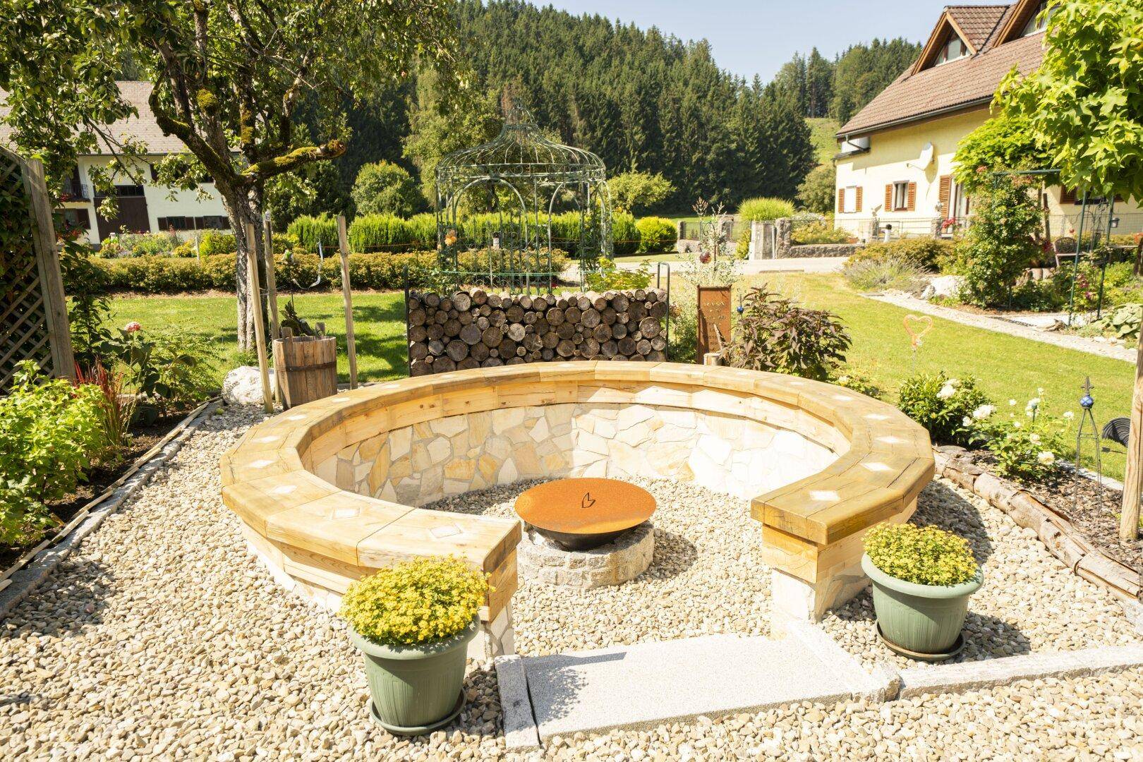 Gemütlicher Feuerstellenbereich im Garten mit Steinsitzgelegenheiten und Kiesboden.