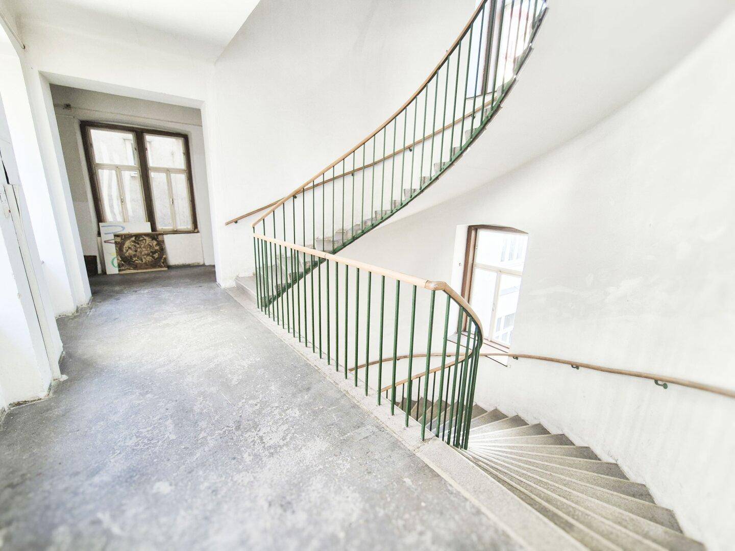 Elegantes Treppenhaus mit geschwungener Treppe, grünem Geländer und hellen Wänden.