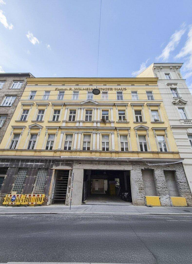 Historische gelbe Fassade eines Gebäudes mit vielen Fenstern und einem großen Torbogen zur Straße.