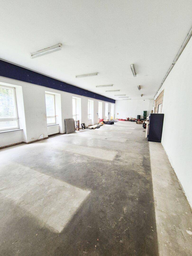 Großer, leerer Gewerberaum mit Betonboden, weißen Wänden und vielen Fenstern, bereit zur Gestaltung.