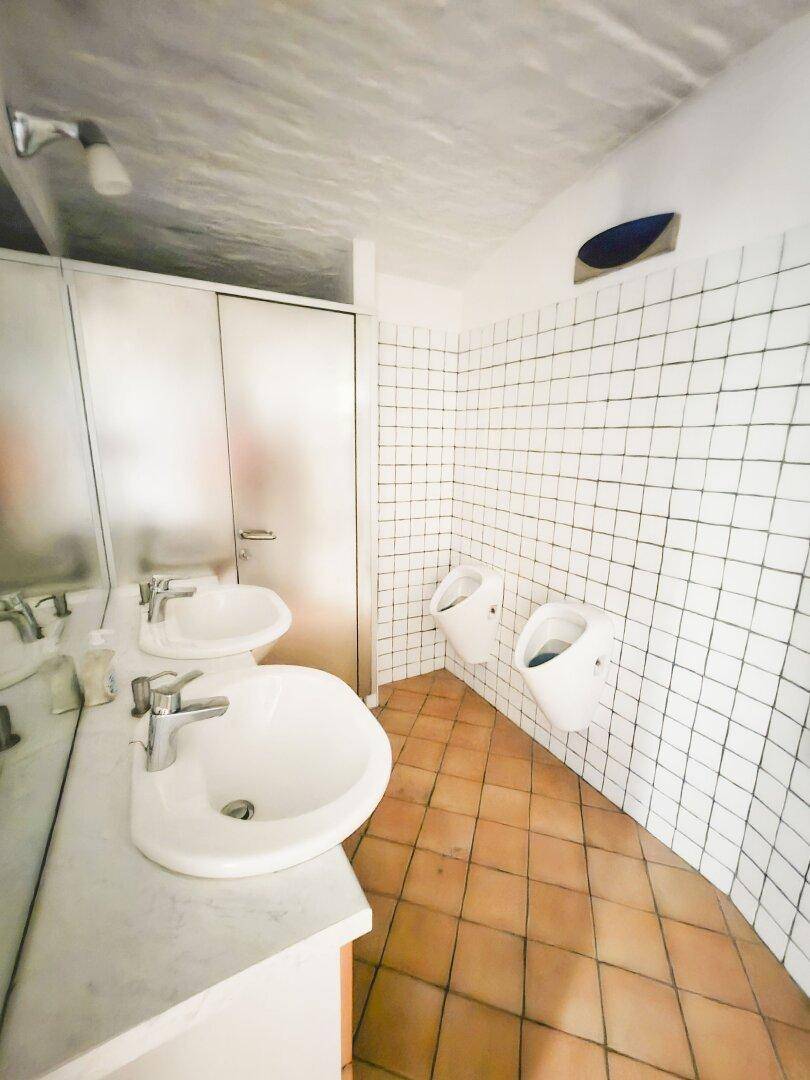 Funktionaler Waschraum mit zwei Waschbecken, zwei Urinalen und gefliesten Wänden und Böden.