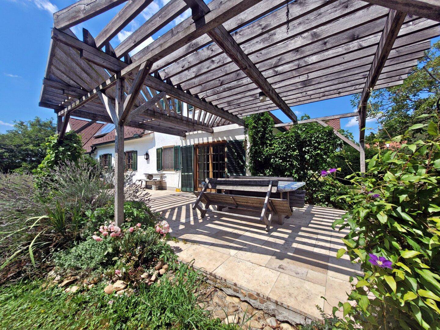 Detailansicht der Holzpergola über der Terrasse mit üppiger Bepflanzung und Sitzbereich.