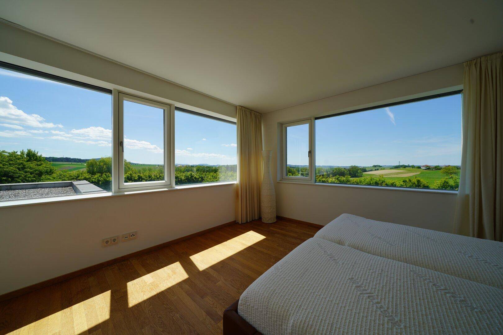 Helles Schlafzimmer mit Holzboden und Panoramafenstern, die einen weiten Blick über die Landschaft bieten.