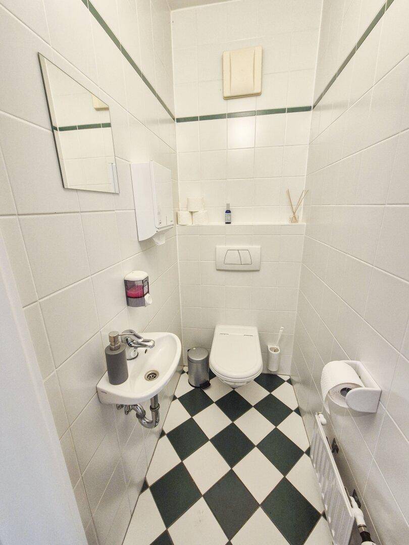 Kleines Gäste-WC mit schwarz-weiß karierten Fliesen, wandhängendem WC und kleinem Waschbecken.