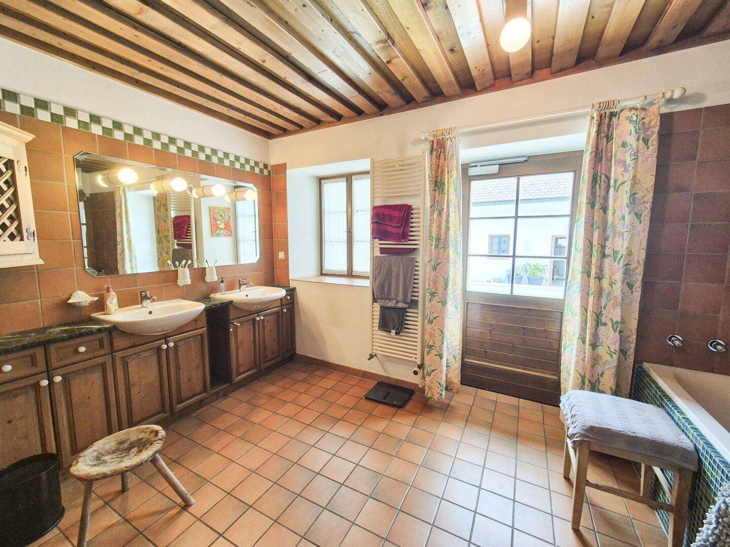 Badezimmer im Landhausstil mit Doppelwaschbecken, Badewanne und Holzbalkendecke.